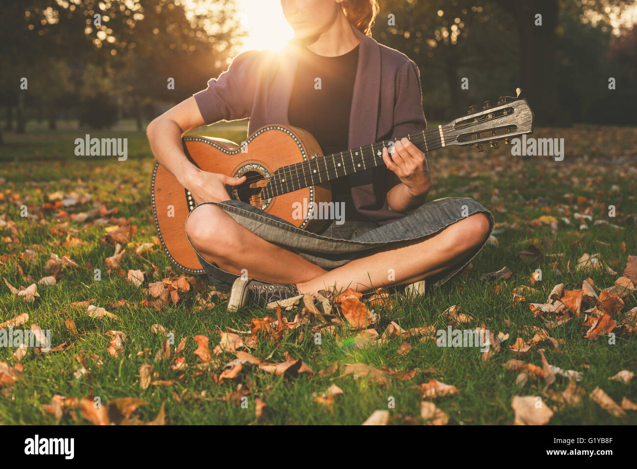 A young woman is sitting on the grass in the park and is playing guitar ...