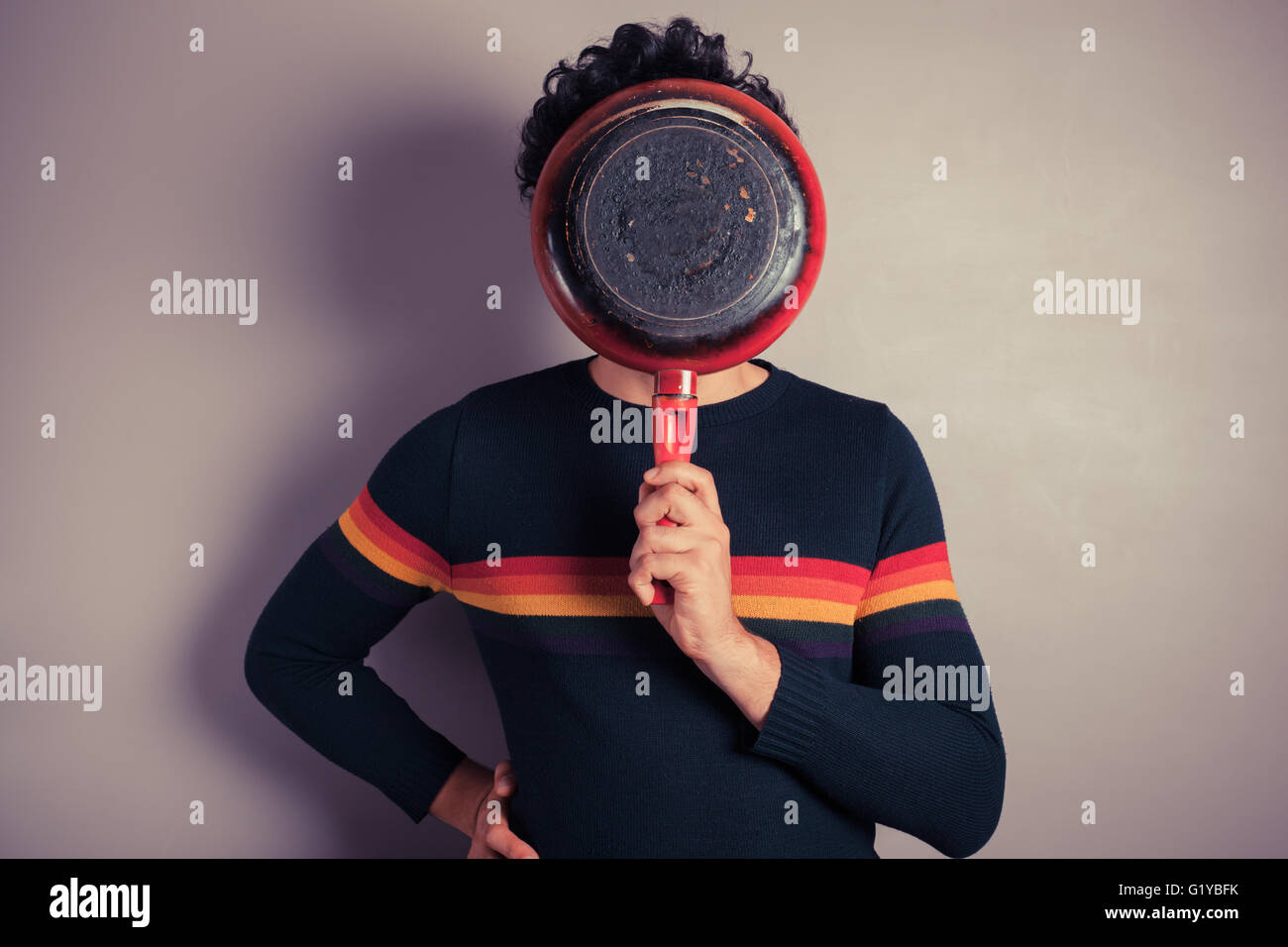 A young man is hiding his face behind a red frying pan Stock Photo