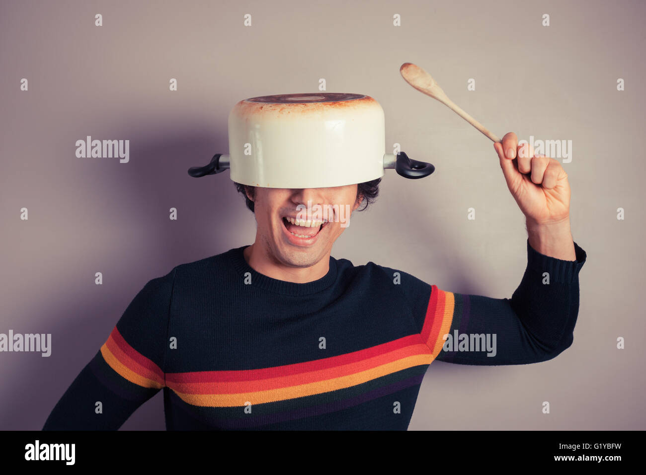 A silly young man is wearing a cooking pot on his had and is holding a ...
