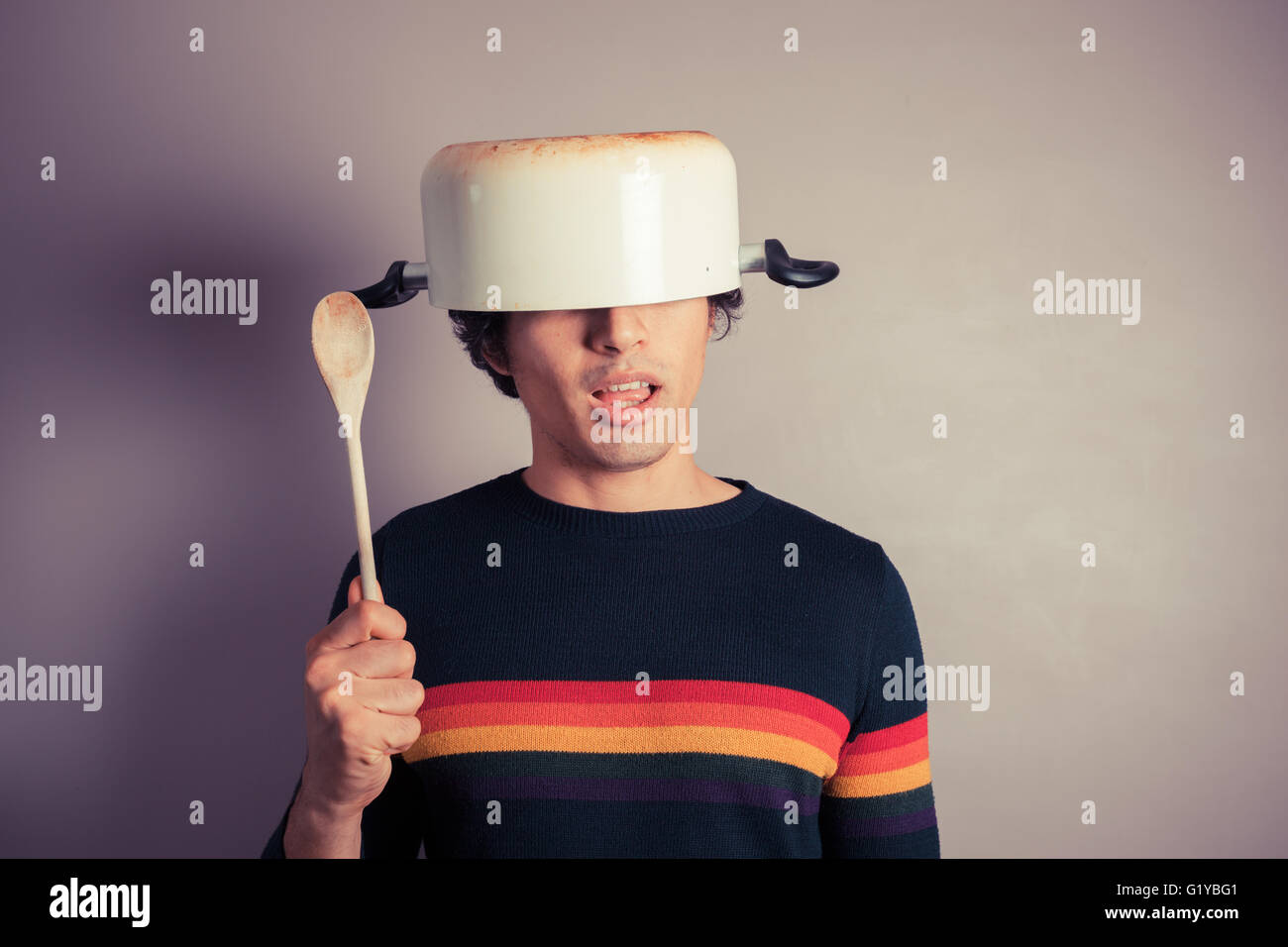A silly young man is wearing a cooking pot on his had and is holding a ...