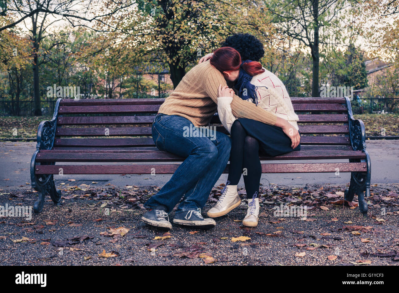 A sad young couple is embracing on a park bench in autumn Stock Photo