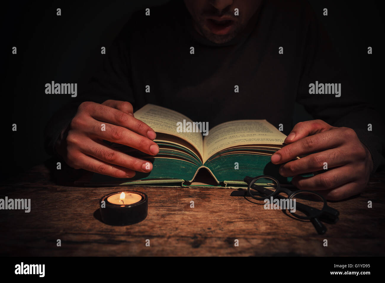A man is reading a big book by candle light at night Stock Photo Alamy