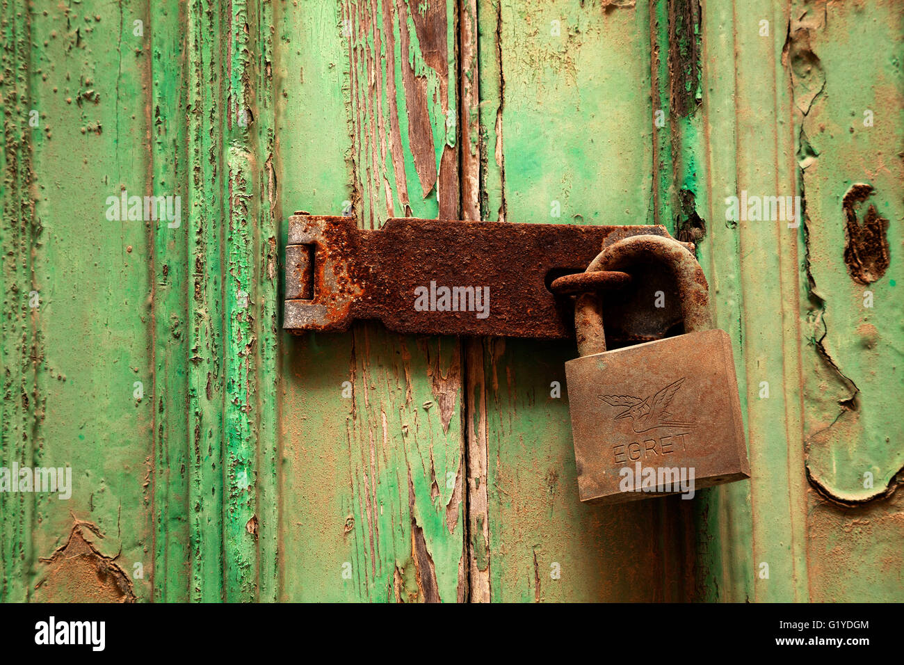 Rusty door lock with deadbolt on weathered wooden door with green paint