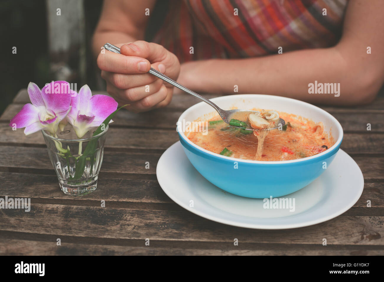 A young woman is eating tom yum soup at a table outside Stock Photo