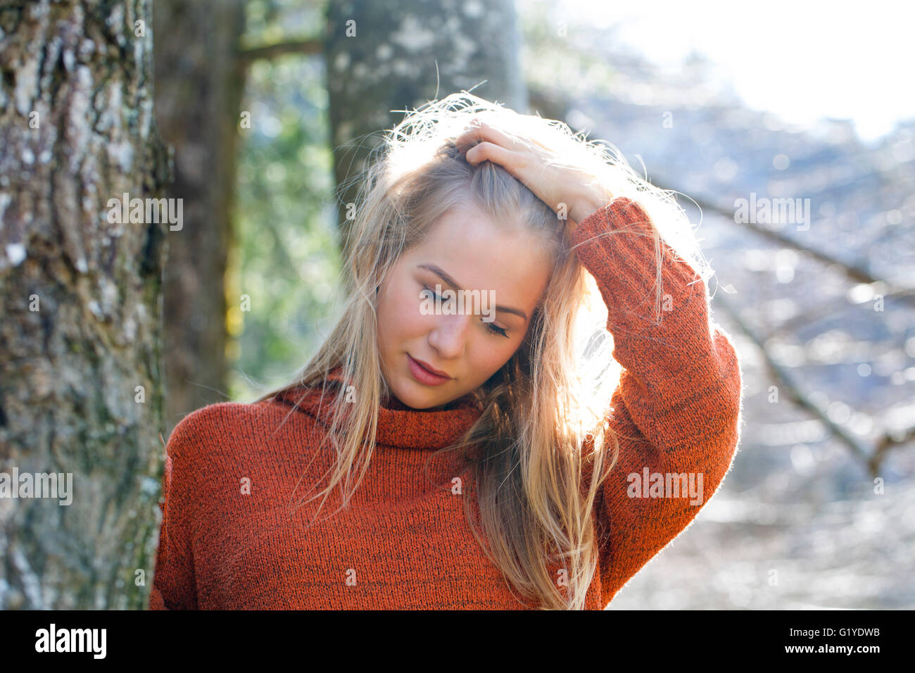 Young girl with long blond hair leaning on a tree Stock Photo