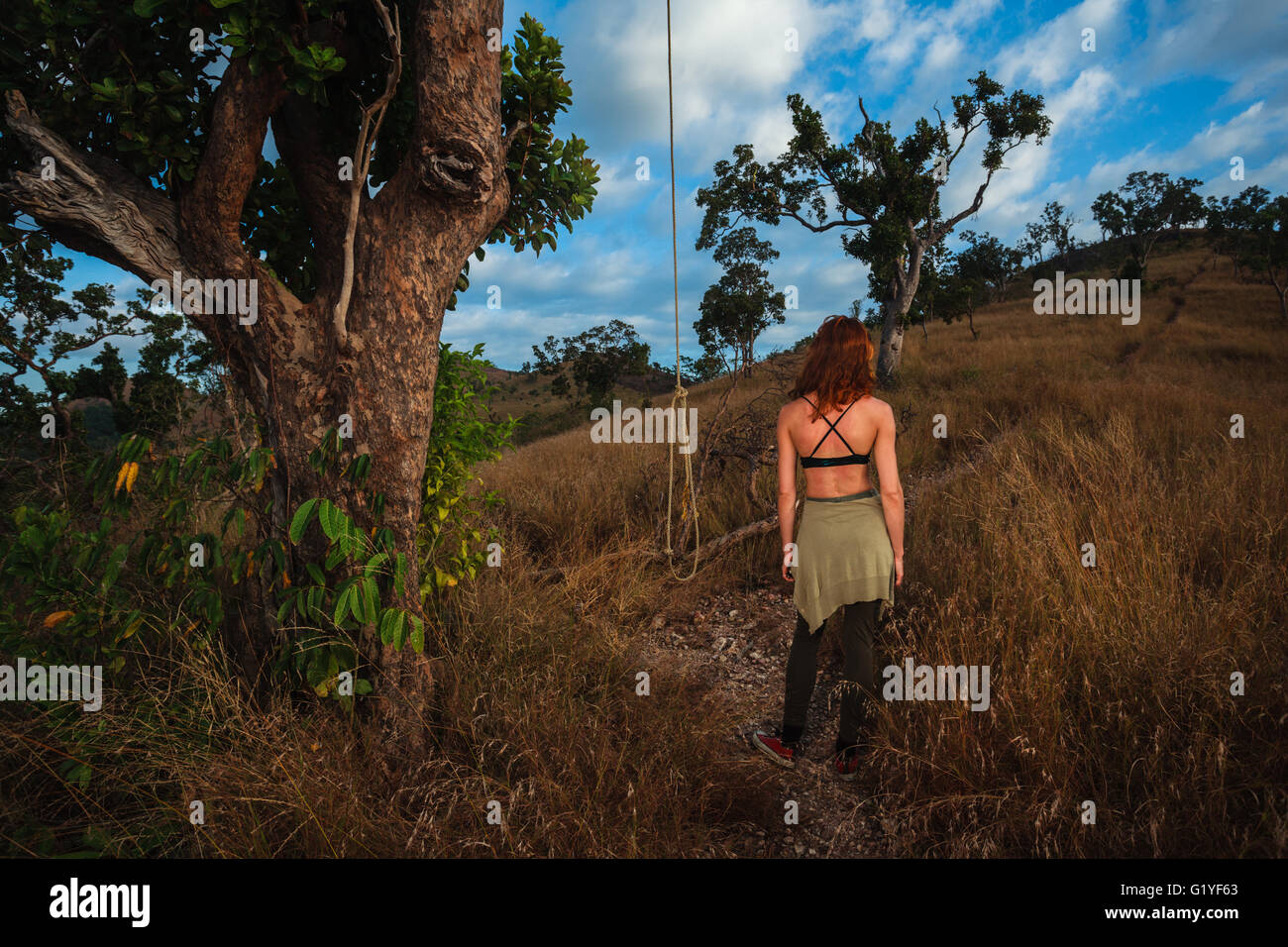 A young woman is standing next to a rope hanging from a tree on a hill Stock Photo