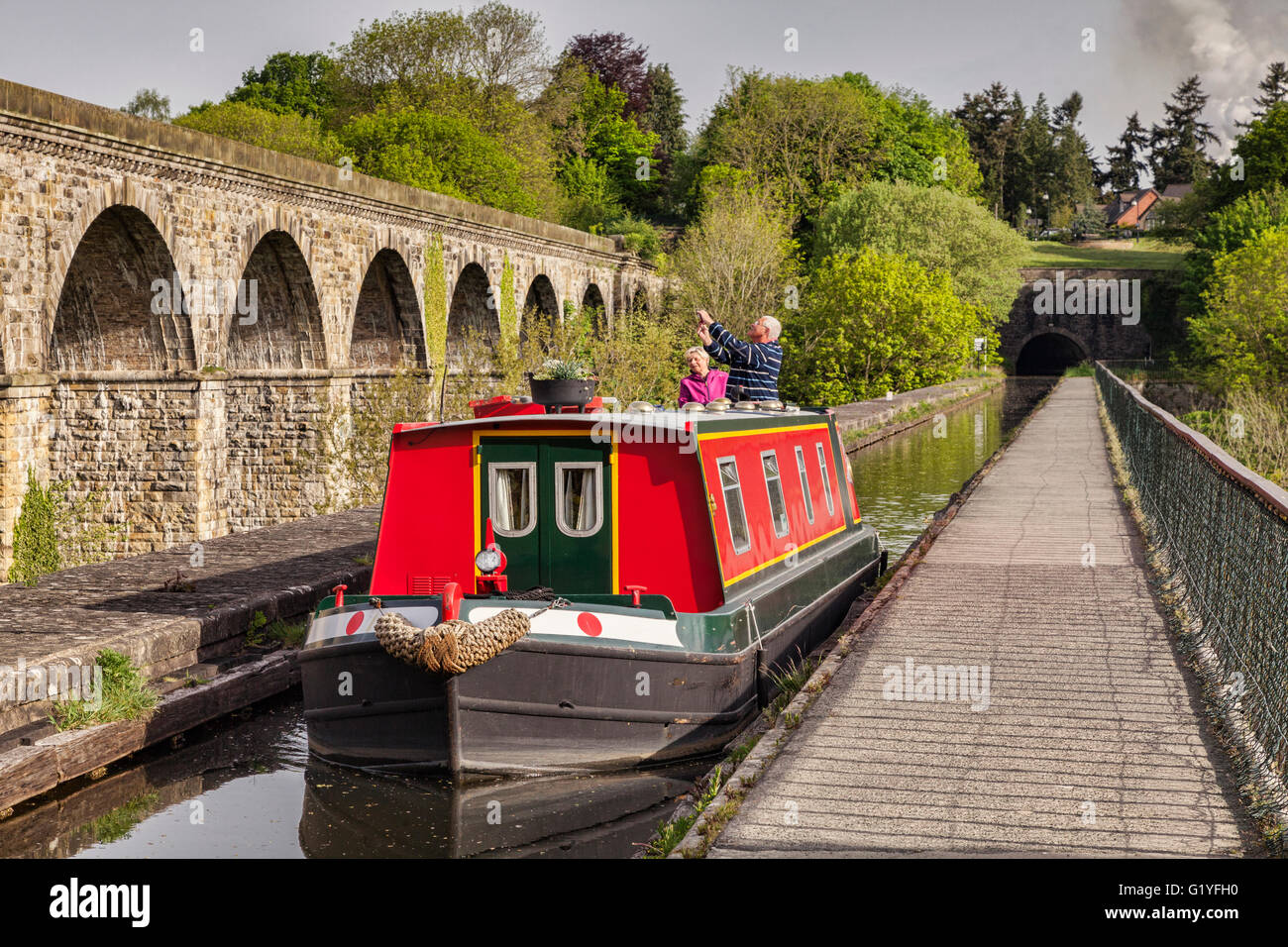 Senior couple in narrowboat crossing Chirk Aqueduct and taking photos of railway viaduct, Chirk, County Borough of Wrexham... Stock Photo