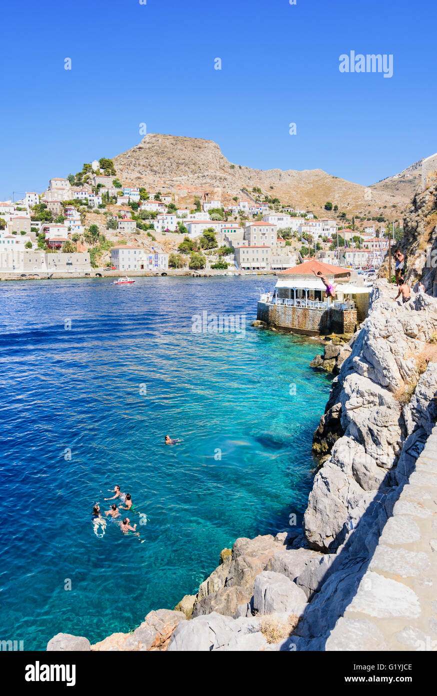 People leaping off rocks into the sea near the rocky Spilia Beach area, Hydra Town, Hydra Island, Greece Stock Photo