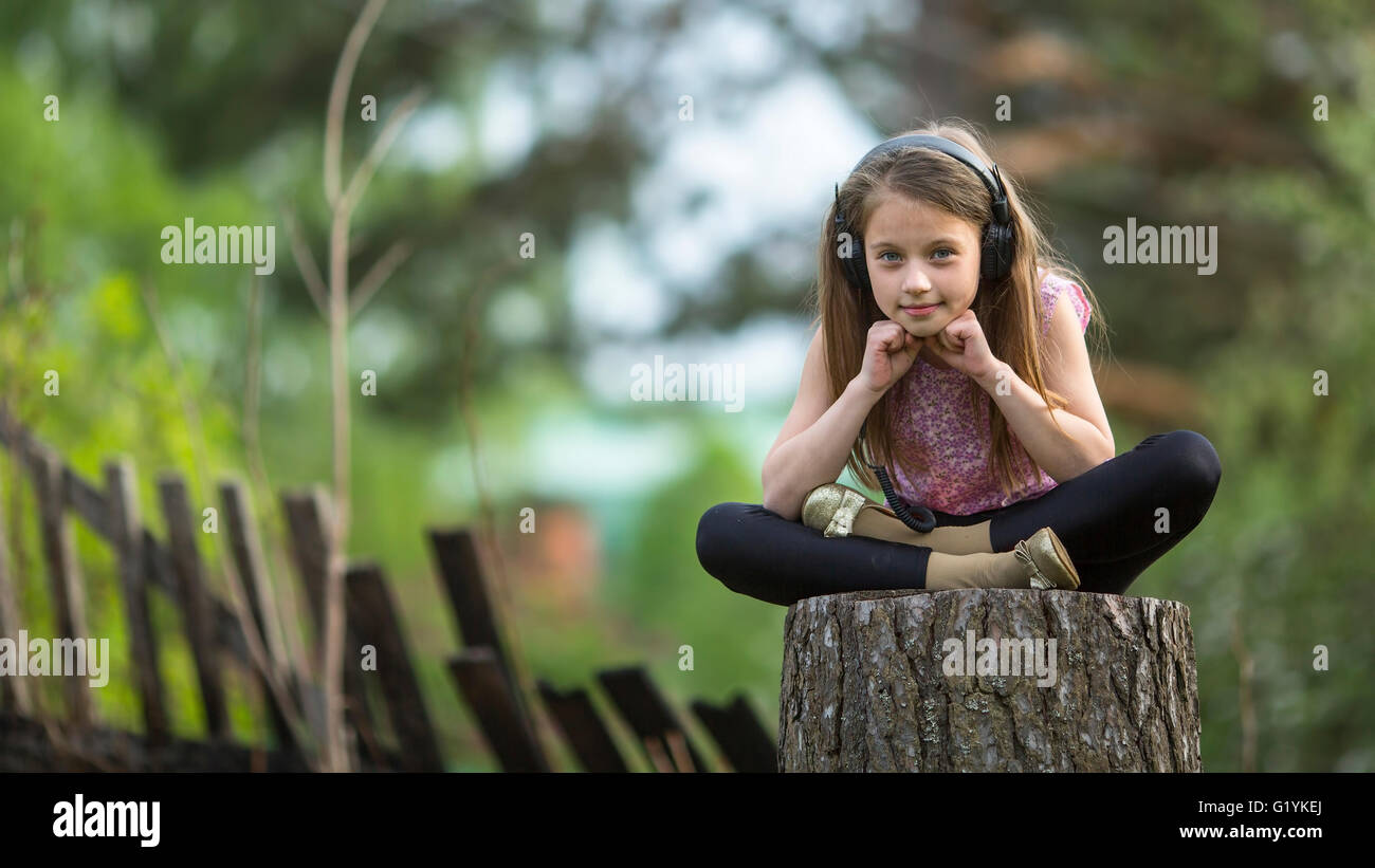 Little girl in headphones sitting thoughtfully outdoors. Stock Photo