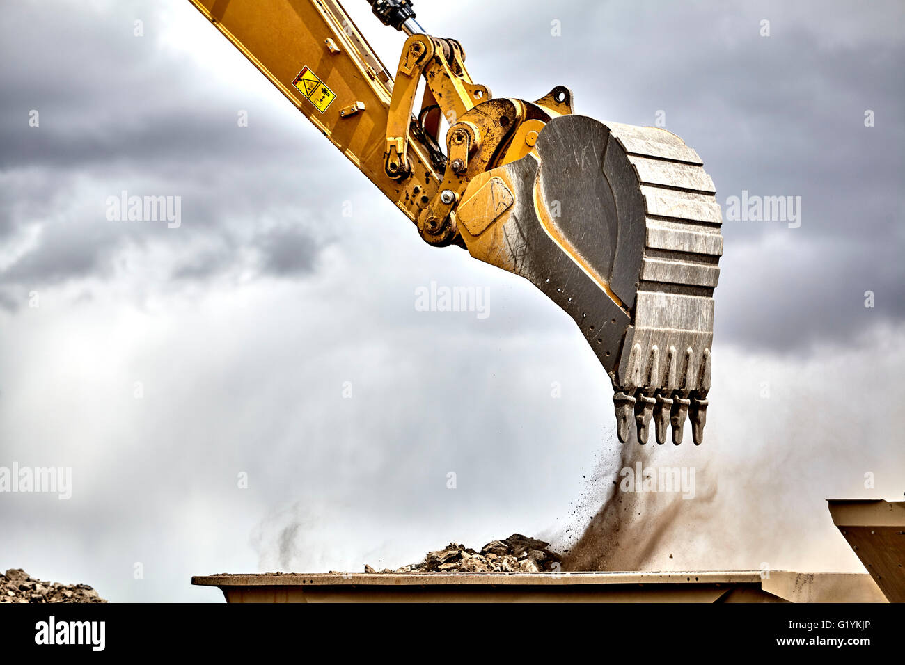 Construction industry heavy equipment excavator moving gravel at jobsite quarry with stormy skies Stock Photo