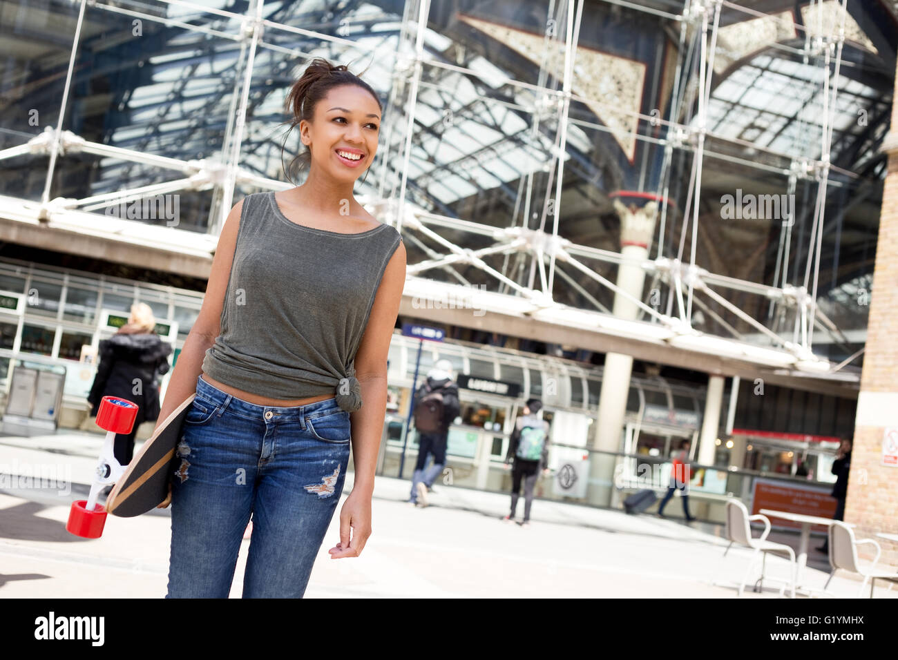 A happy young woman holding a skateboard in the city. Stock Photo
