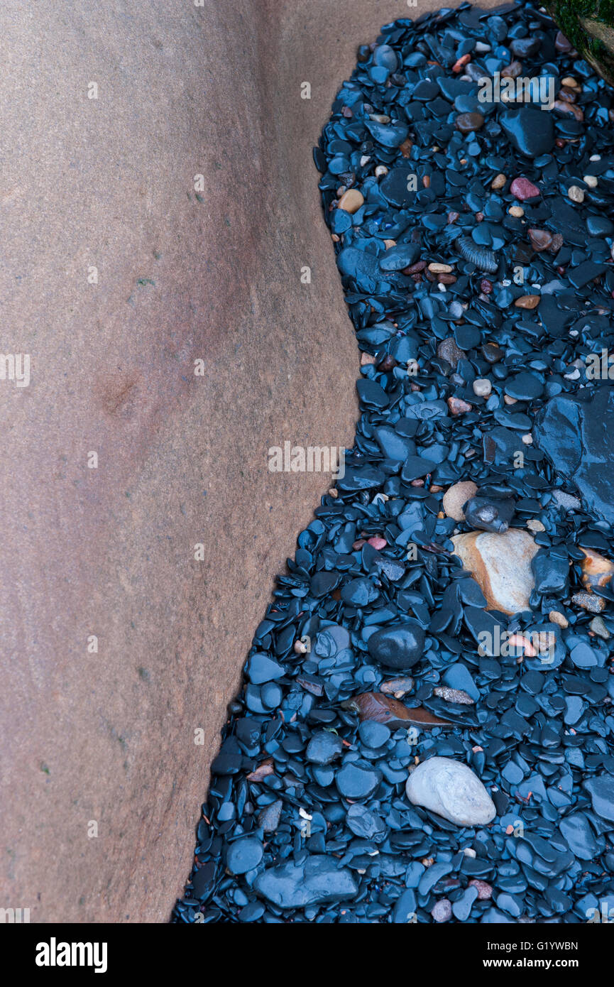 Contrasting colours seen in a close-up of dark, wet, shiny, beach pebbles and a large white rock - Yorkshire, England. Stock Photo