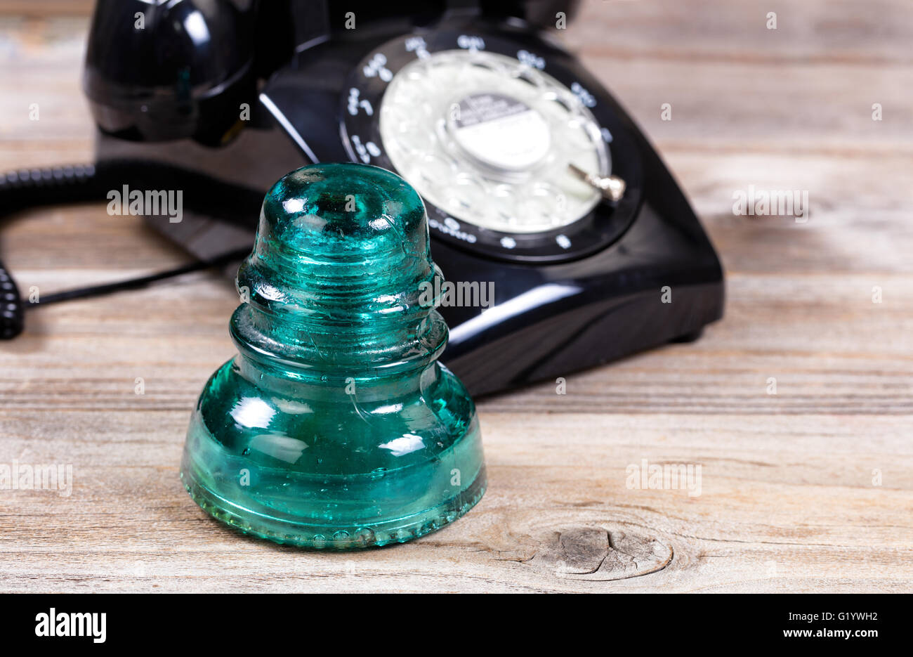Close up of an antique electric glass insulator with vintage manual dial phone in background. Stock Photo