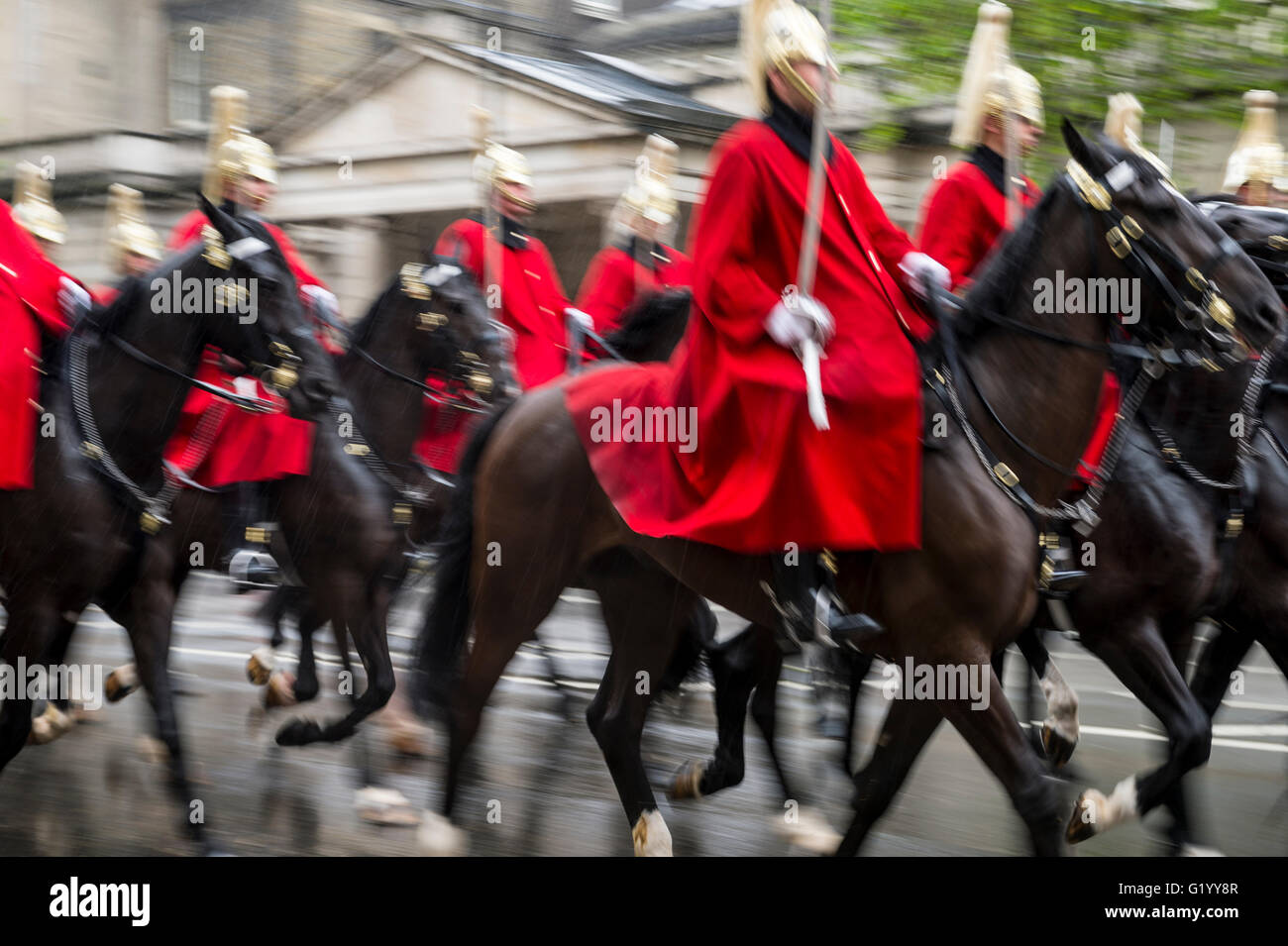 Royal guards on horseback dressed in ceremonial red coats pass in a parade on a rainy day in