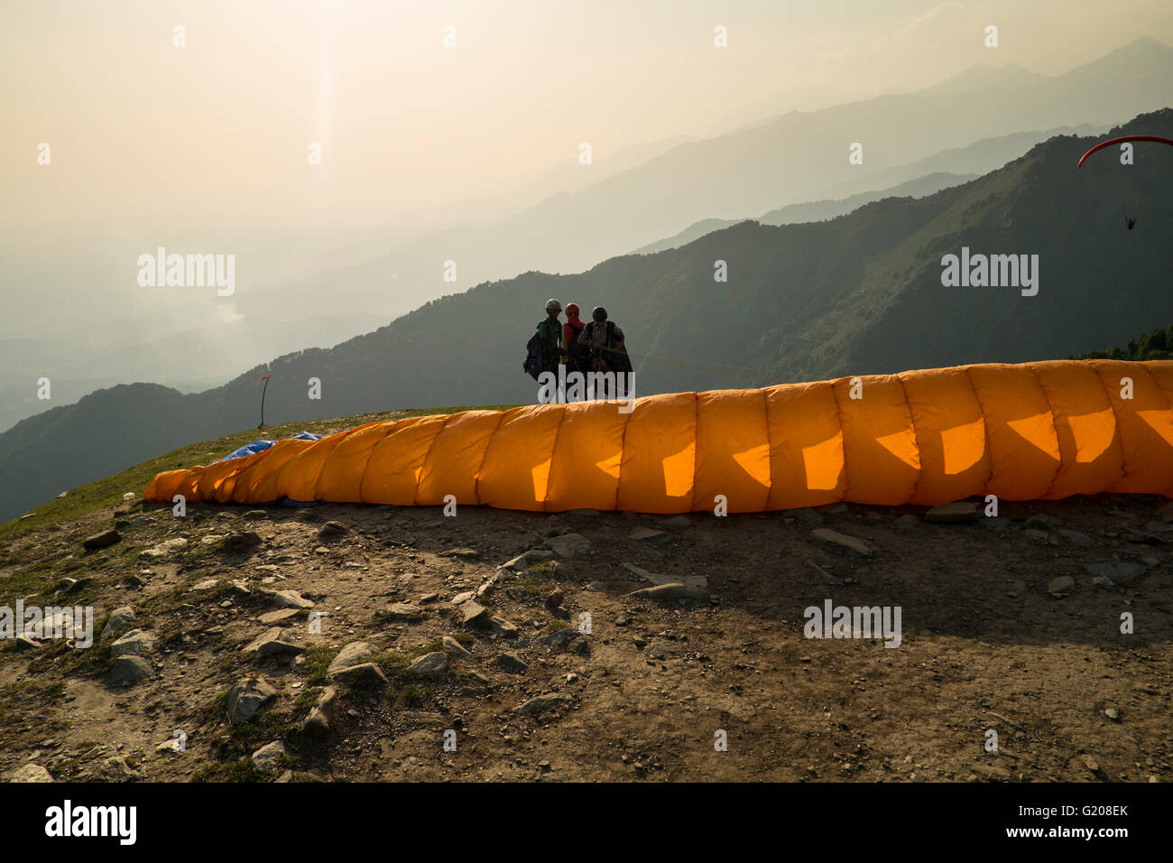 A paraglider starts catching the wind in its wings as the flyers are caught in a silhouette in Bir Billing, Himachal Pradesh, In Stock Photo