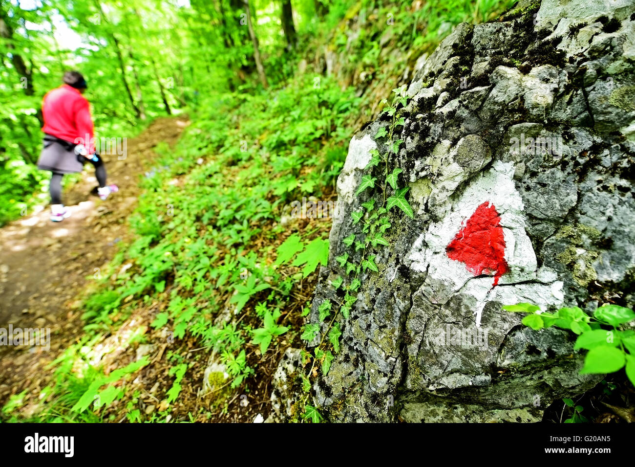 Hiking red triangle paint marking on a rock with hiker on the trail Stock Photo