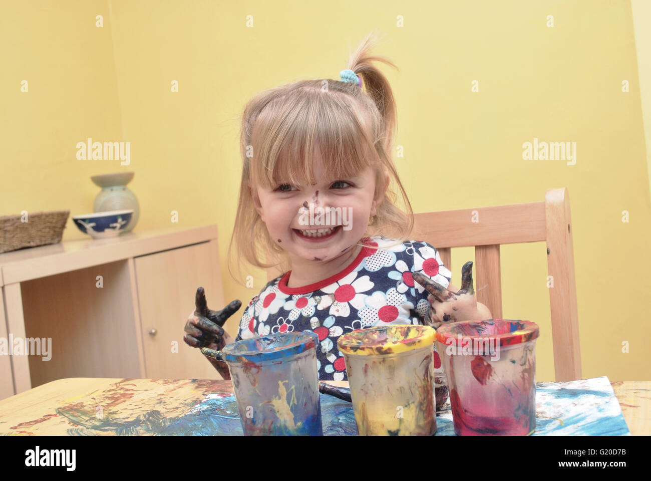 A happy three year old little girl painting at the table in the home