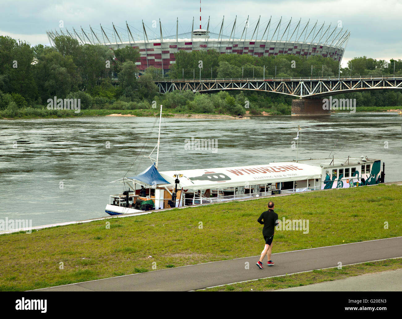 man jogging past a restaurant boat on the river Vistula Warsaw Poland with the national stadium in the background Stock Photo