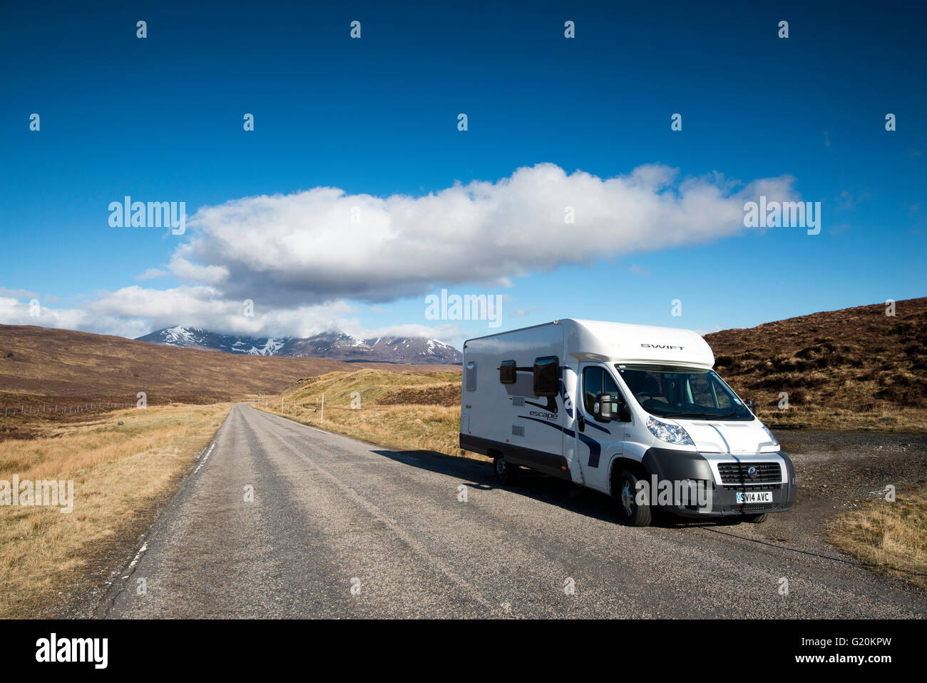 A motorhome surrounded by fluffy white clouds and endless open road on the A832 in the far North West of Scotland, UK Stock Photo