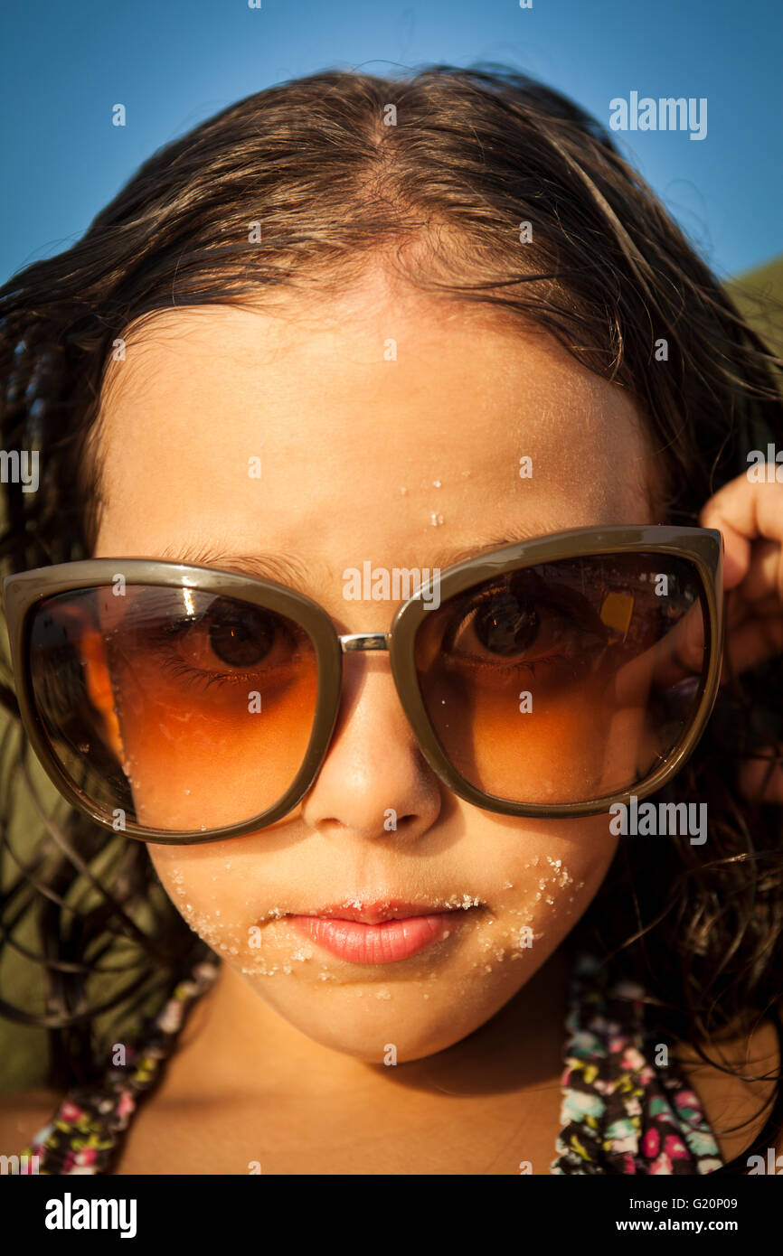 cute young girl wearing big sun glasses while looking at the lens at a  bright summery day, Greece Stock Photo - Alamy