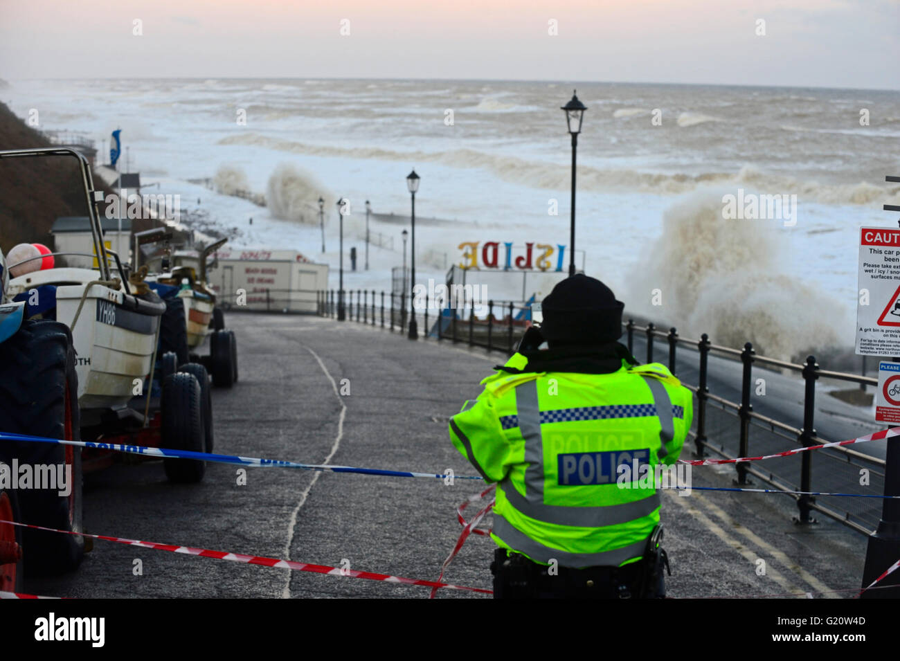 Police officer taking a picture on her mobile phone of rough seas during storm surge on Cromer seafront Norfolk Dec 2013 Stock Photo