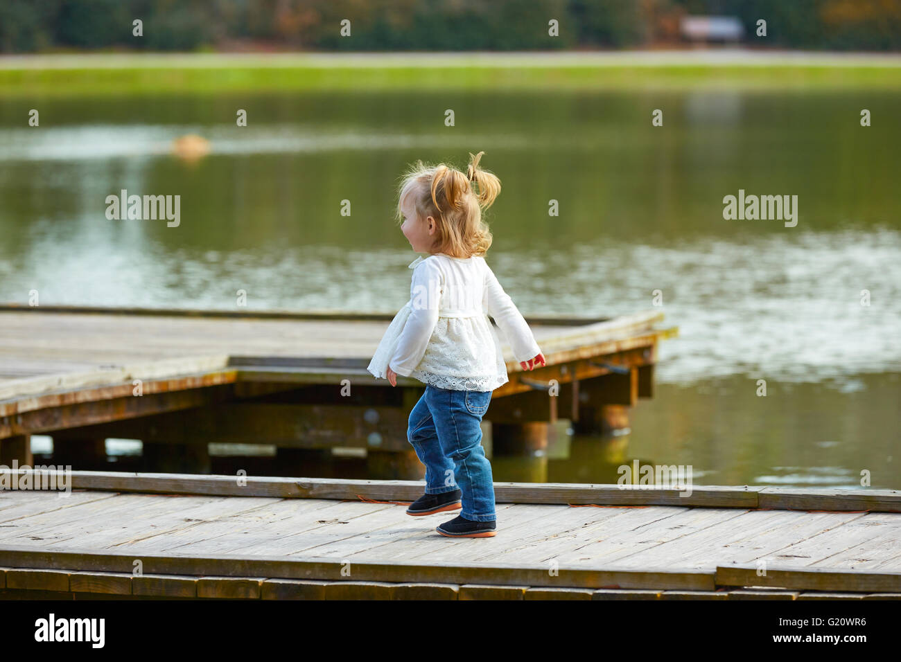 Blond Kid girl walking in the lake pier at the park Stock Photo - Alamy
