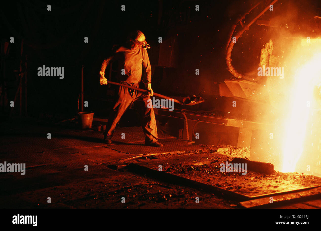 Germany - Velbert, Krupp steel production. Worker wearing protective gear operates near kiln with molten steel Stock Photo