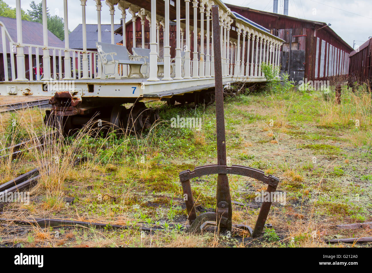 Rusting rail yard switch in overgrown field with rusting railroad cars. Stock Photo