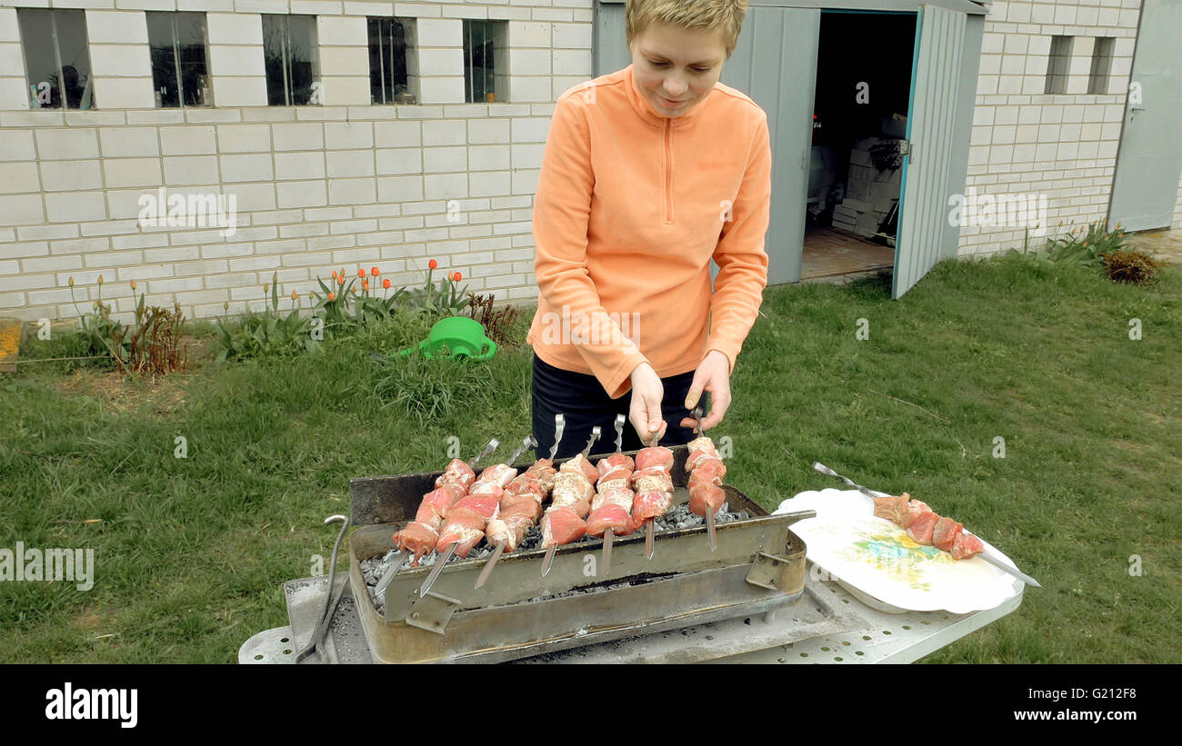 Girl cooks barbeque skewers with meat on brazier Stock Photo