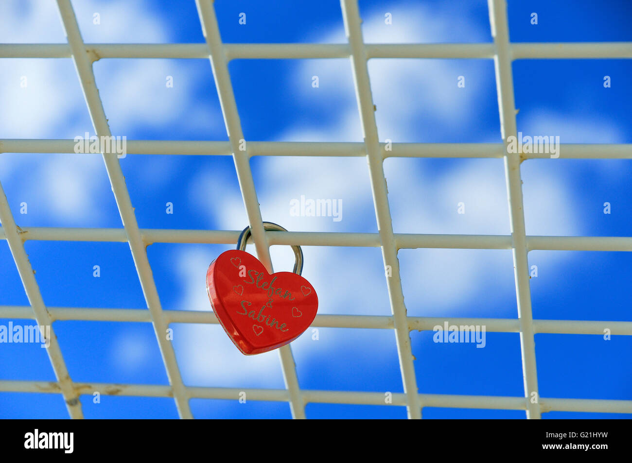 Red padlock, heart shaped, love lock on grid in frint of blue sky, Lower Saxony, Germany Stock Photo