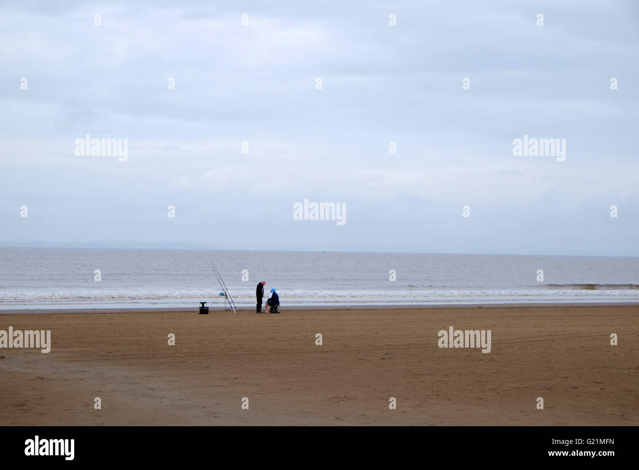 Two people fishing at the shore line on the beach at Weston super Mare