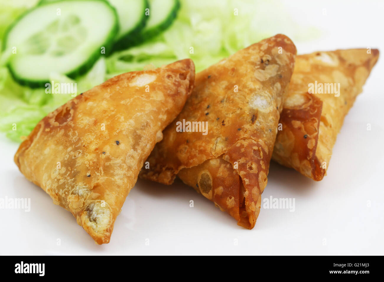 Three Indian samosas with green lettuce and slices of cucumber on the side, closeup Stock Photo