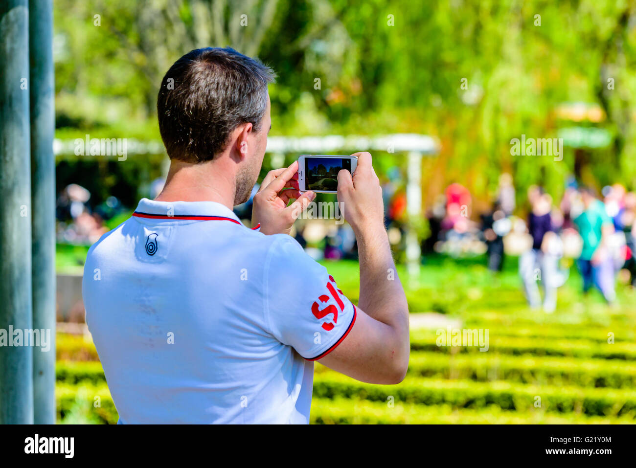 Ronneby, Sweden - May 8, 2016: Male person taking a photograph using his white mobile telephone. People and vegetation blurred o Stock Photo