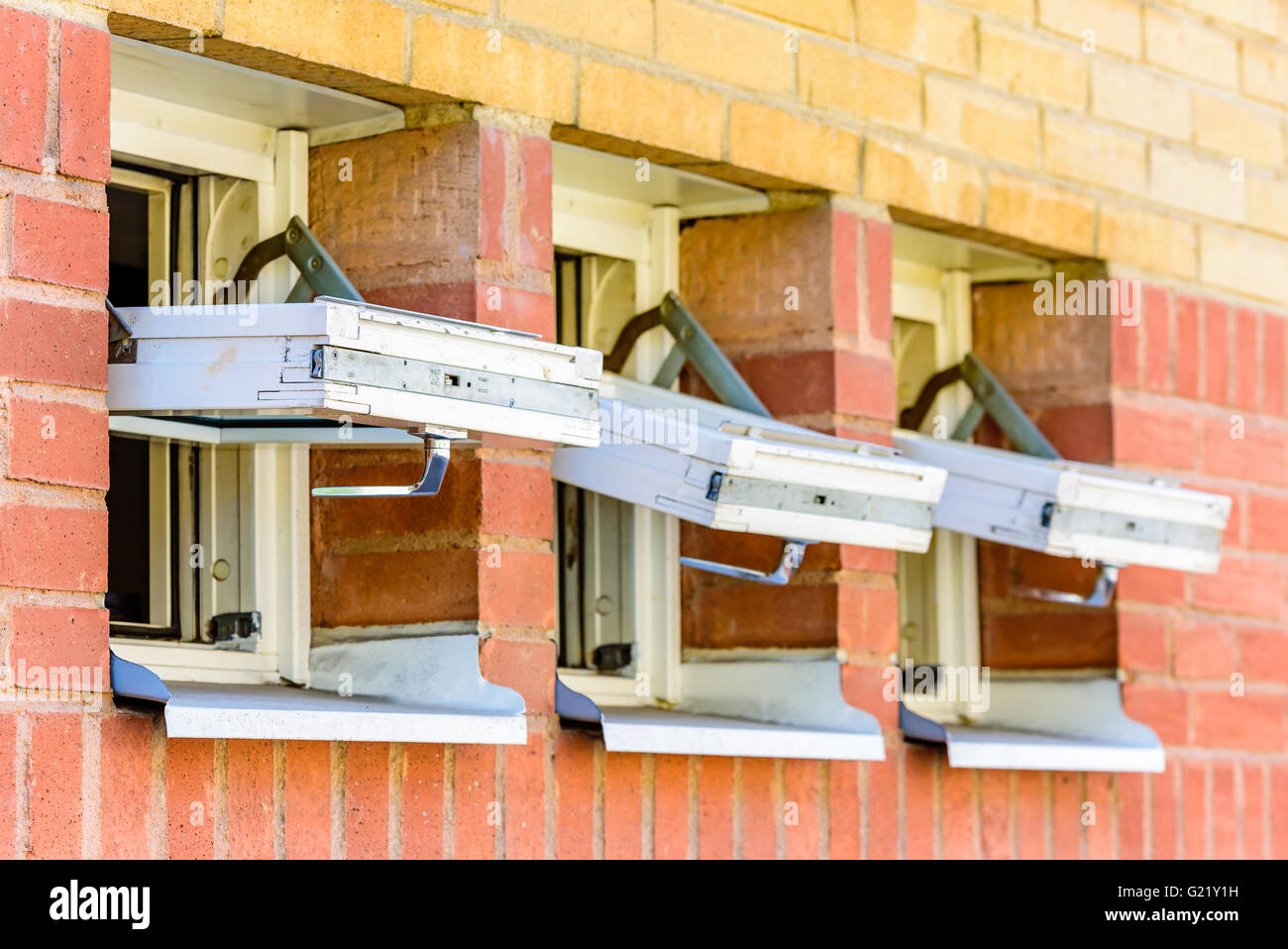 Three small open windows on a red and yellow brick building. Stock Photo