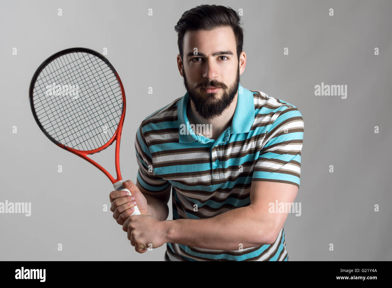 Concentrated tennis player in polo shirt holding racket with both hands ...