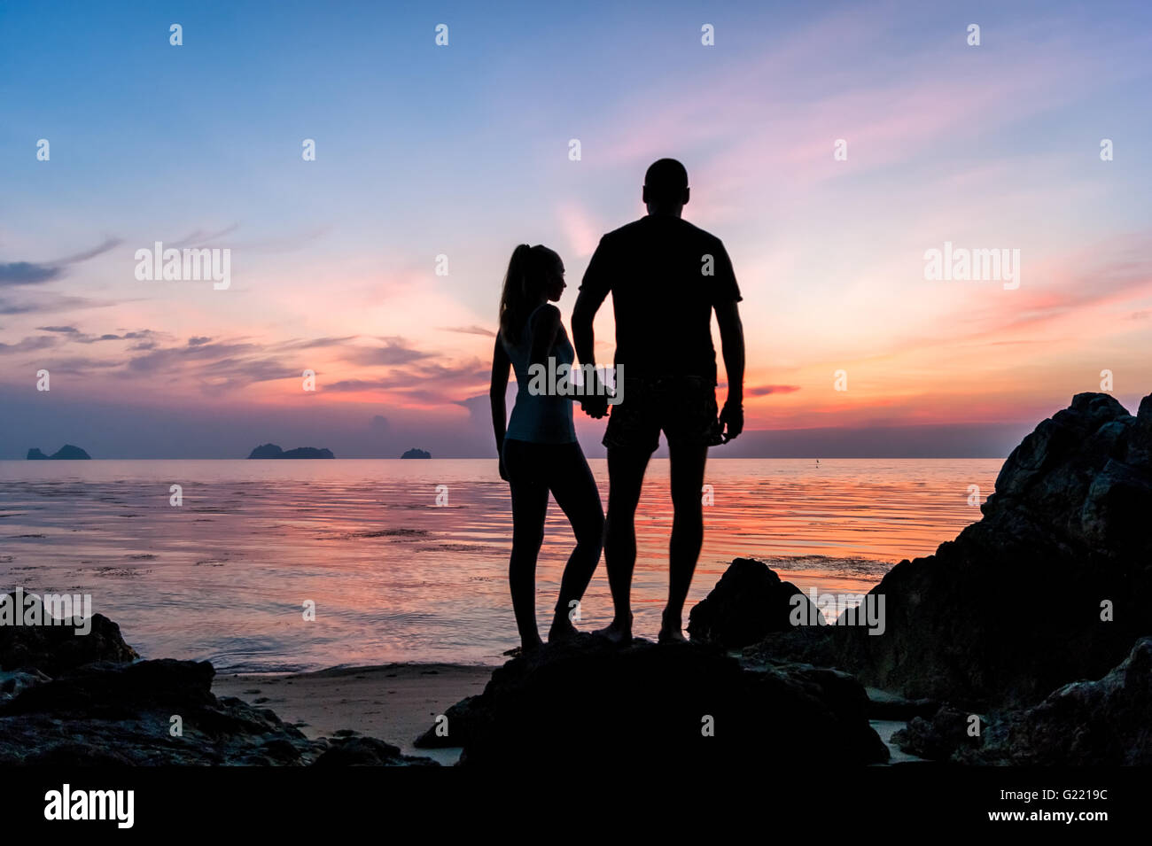 Silhouette young couple standing on the beach holding hands and ...