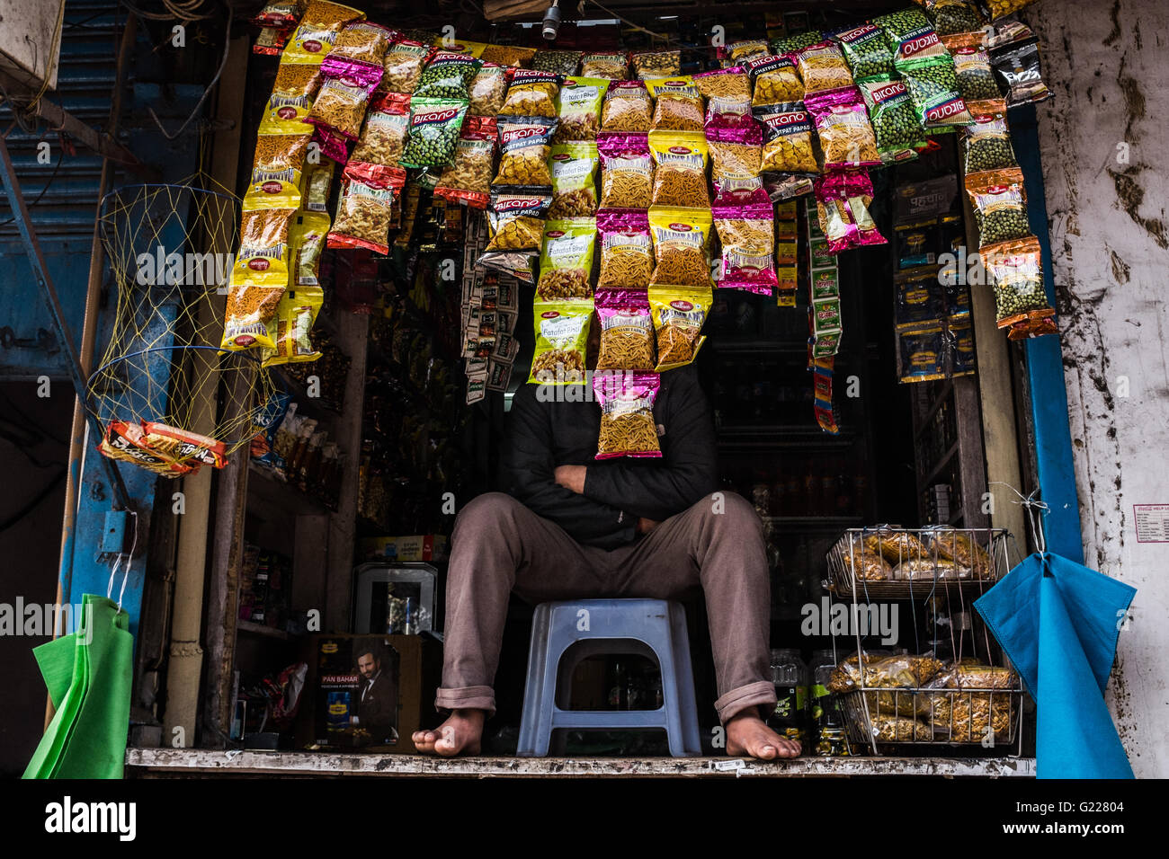 Man sat behind display of packages of food in Delhi, India. Stock Photo
