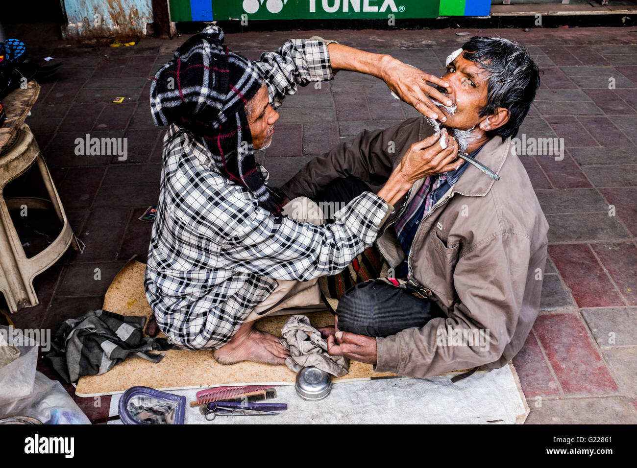 Street barber shaving man on streets of Delhi, India Stock Photo