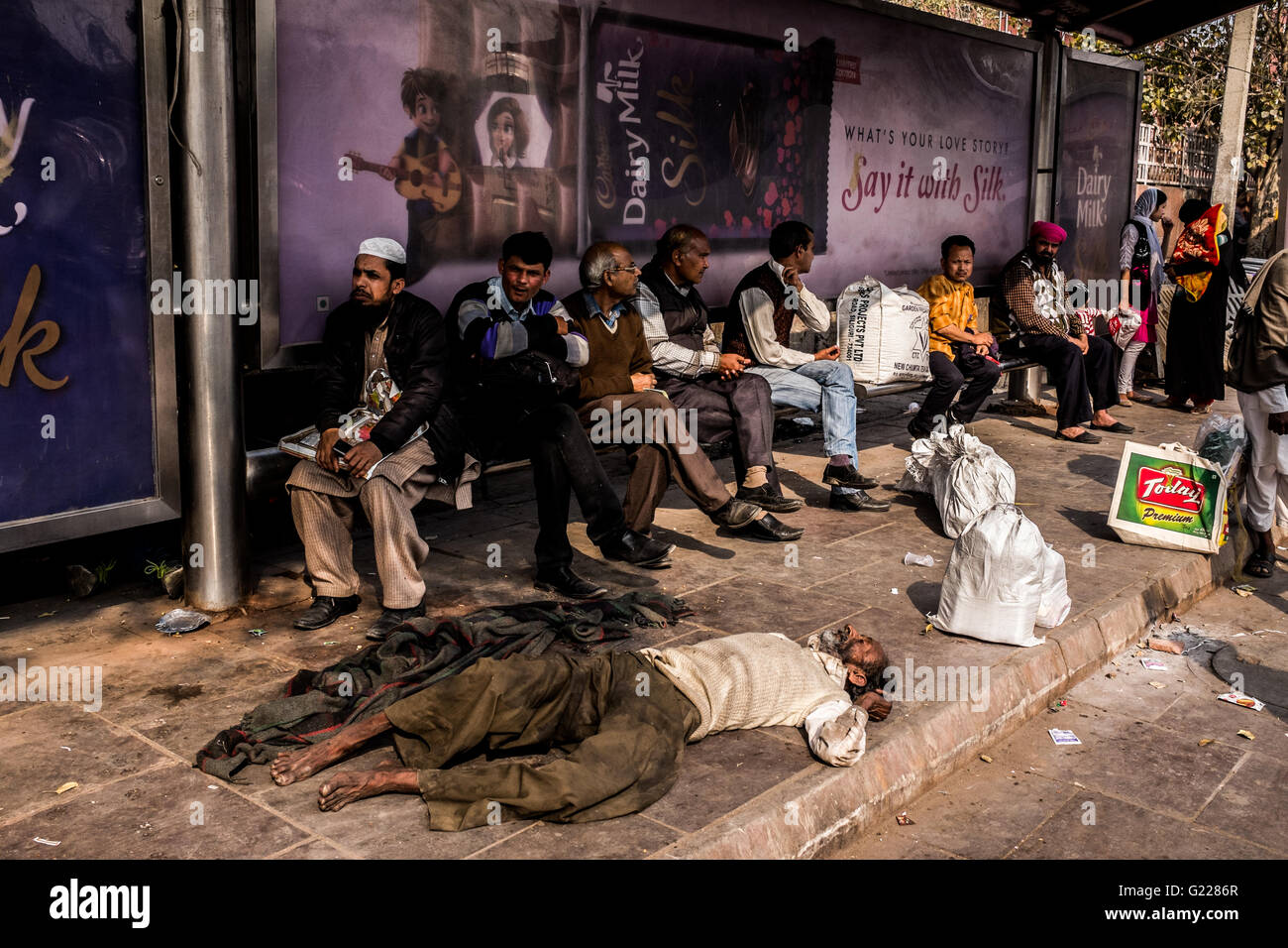 Man passed out on floor as other people wait at a bus stop in Delhi, India Stock Photo