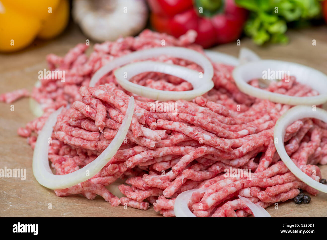 Raw minced meat and onion rings close-up with fresh vegetables on the background Stock Photo