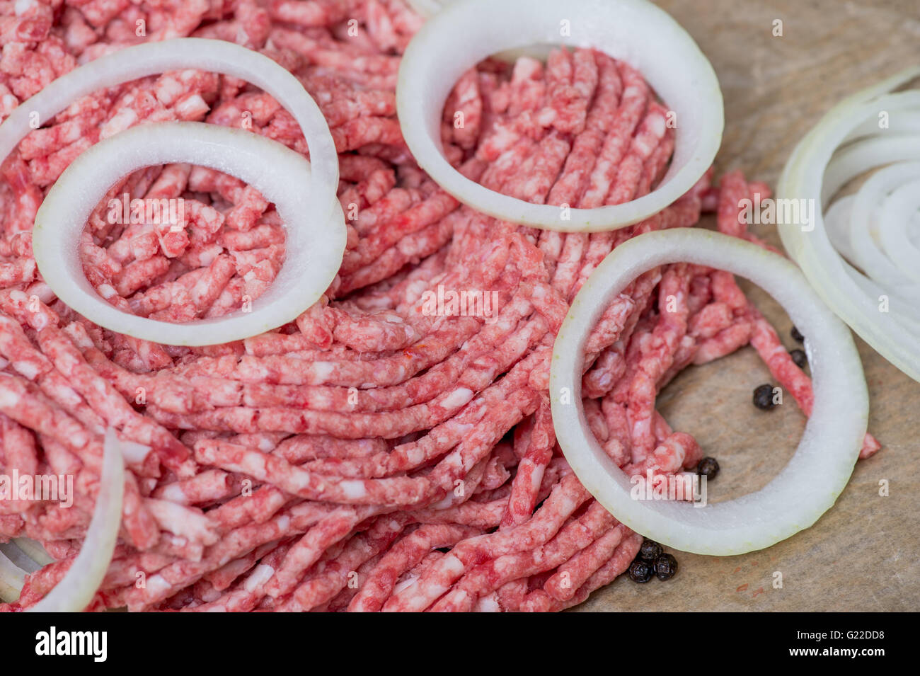 Raw minced meat and onion rings close-up with fresh vegetables on the background Stock Photo