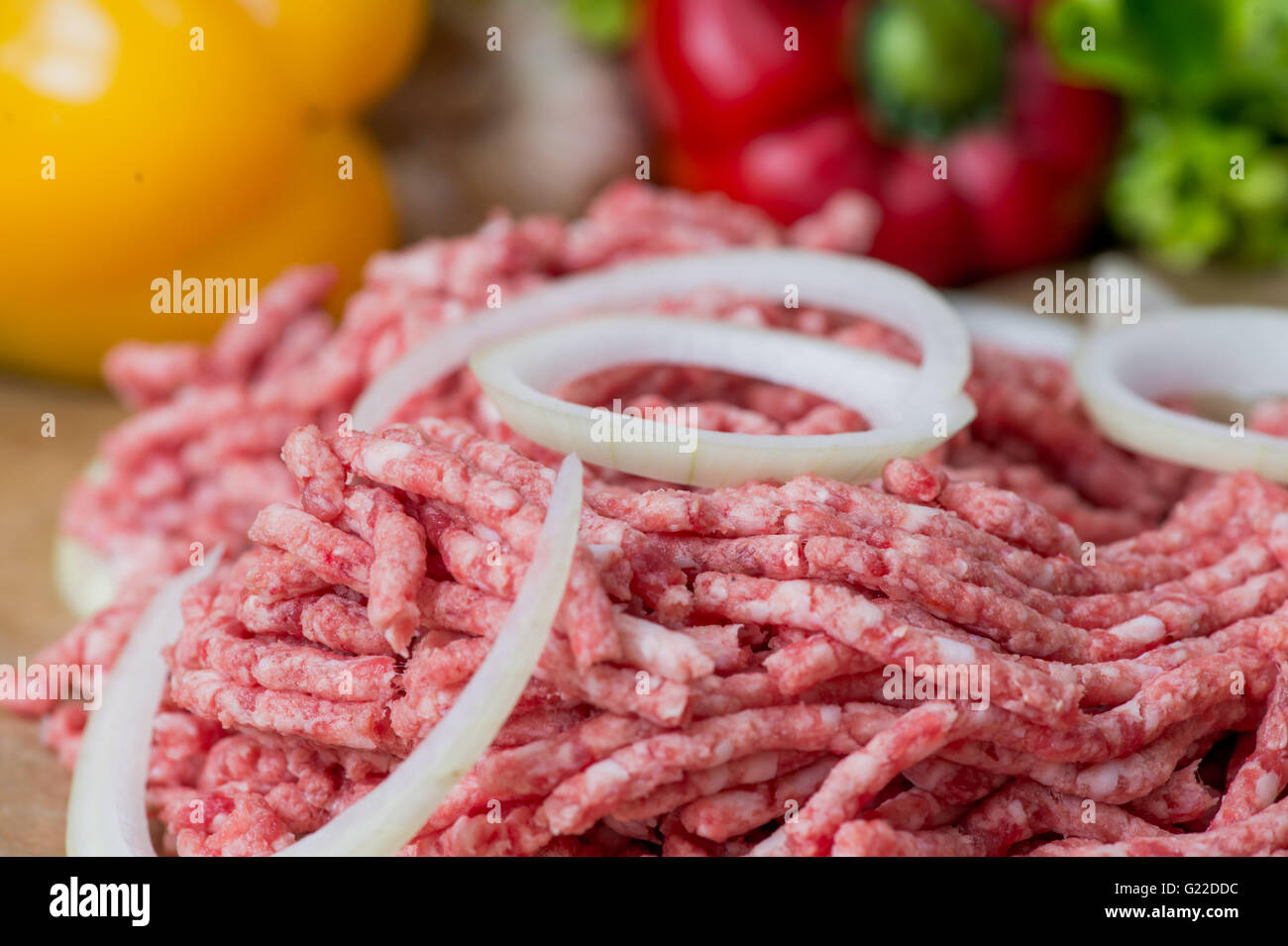 Raw minced meat and onion rings close-up with fresh vegetables on the background Stock Photo
