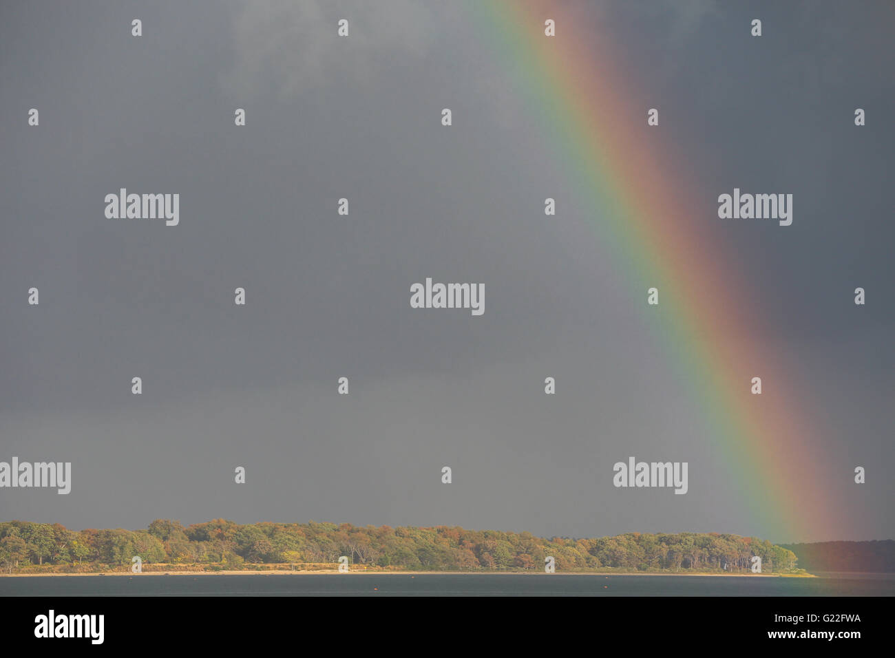 rainbow in a dark sky over a pristine wooden landscape with water Stock Photo