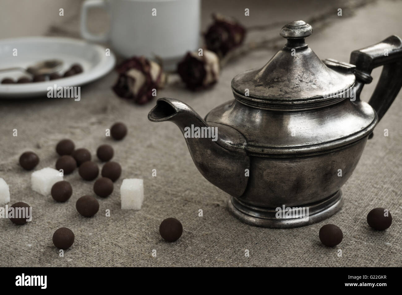 Ancient silver teapot, sugar cubes and chocolate dragees on canvas
