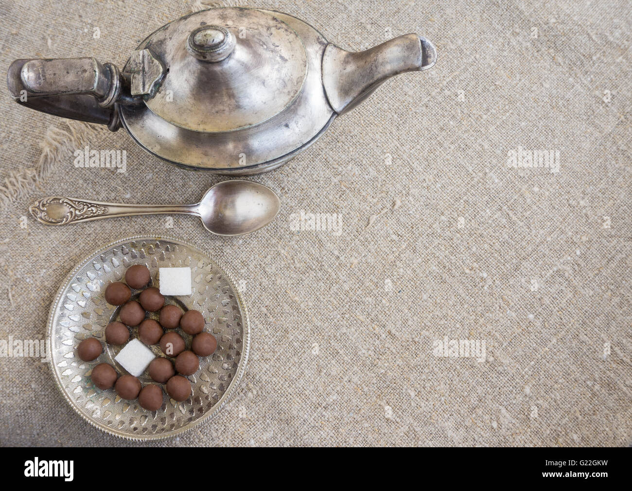 Ancient silver teapot, sugar cubes and chocolate dragees on canvas