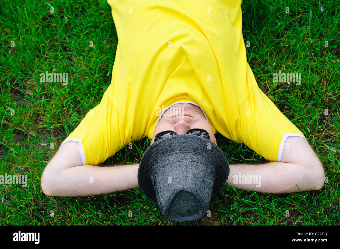 man in yellow T-shirt and hat lying on green grass at park Stock Photo