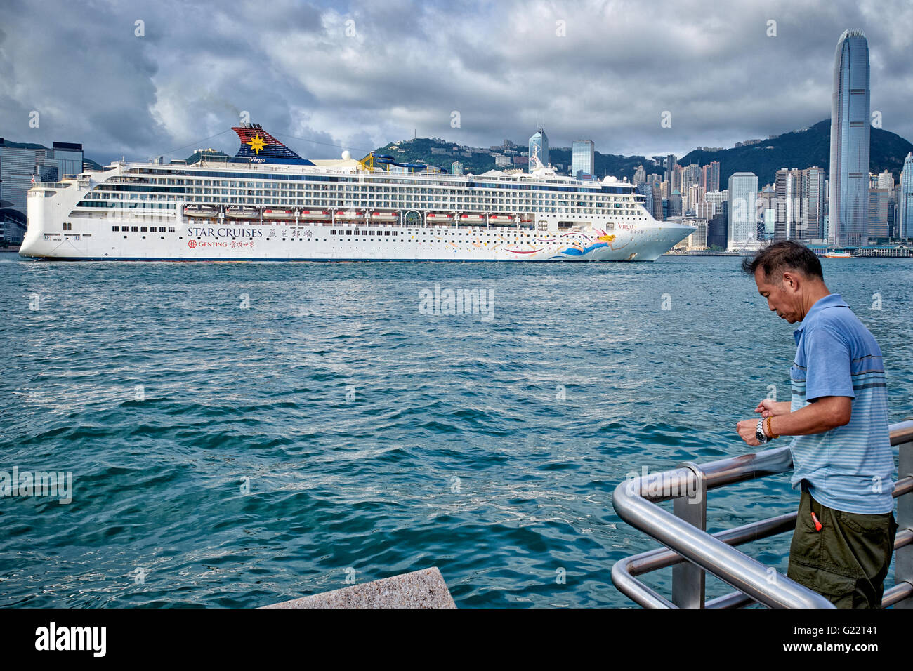 HONG KONG, VICTORIA HARBOUR: A man is handline fishing at the side of Victoria Harbour while a luxury cruise liner passes by. Stock Photo