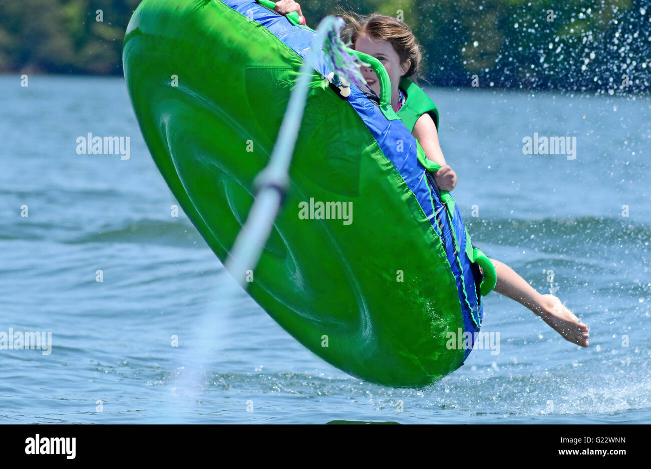 A young girl hanging onto a tube behind a boat as it flies up into the air. Stock Photo
