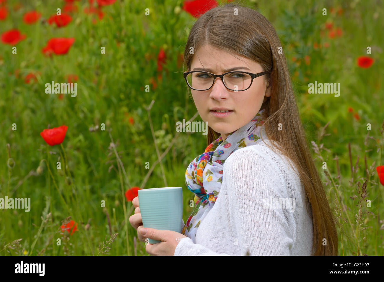 Teen girl drink cup of tea on poppy field Stock Photo