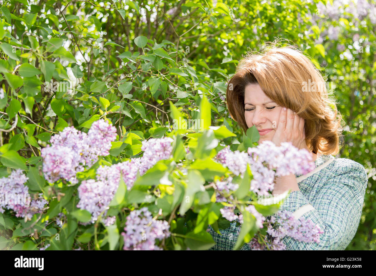 Woman suffering from migraine about blooming lilac Stock Photo